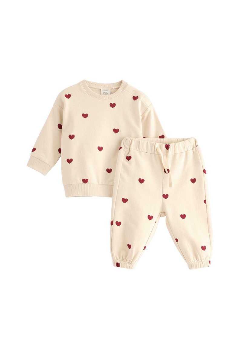 Beige bomullströja och matchande byxor med röda hjärtformat. Tröjan har långa ärmar och ribbade ärmslut; byxorna har midjeband med resår.