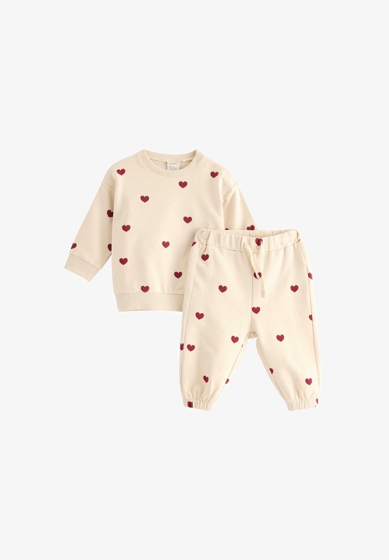 Beige cotton sweatshirt and matching pants with red heart patterns. Sweatshirt has long sleeves and ribbed cuffs; pants have elastic waistband.
