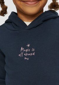 Granatowa bluza z kapturem o miękkiej teksturze z różowym haftem, na którym widnieje napis "Magia jest wszędzie wokół mnie" oraz mała gwiazdka nad napisem.