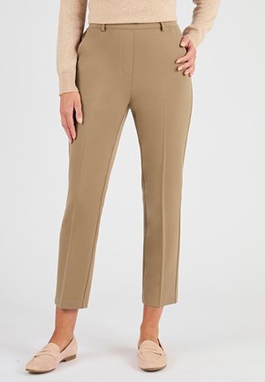 Pantalons beiges sur mesure avec une texture lisse, coupe ajustée et poches avant. L'association avec des mocassins rose clair complète le look.