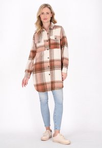 Mønstret skjorte i creme, orange og brune farver; har en knap-åbningsforklæde, to brystlommer og lange ærmer. Bæres med lyse jeans og sneakers.