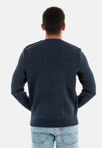 Maglione lavorato a maglia blu navy con scollo rotondo, polsini e orlo a coste, che mostra un tessuto texturizzato e una vestibilità regolare visto da dietro.