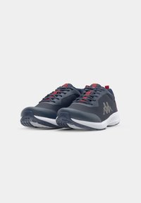Sports shoes featuring a dark blue synthetic upper, red accents, textured material, lace closure, and white cushioned sole with traction design.