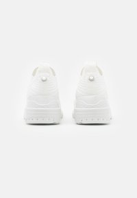 White athletic shoes with a textured upper, pull tabs, and a distinct heel design. Features decorative hardware on the back.