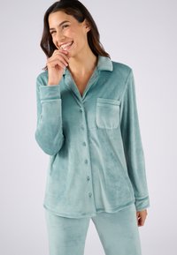 Mintgroene, pluizige pyjama set met een knoopsluiting bovenaan, een borstzak en lange mouwen, gecombineerd met bijpassende broek. Zachte, gladde textuur.