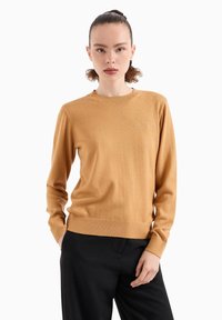 Maglione color senape in tessuto leggero, con maniche lunghe, scollatura rotonda e polsini e orlo a coste. Design semplice e aderente.