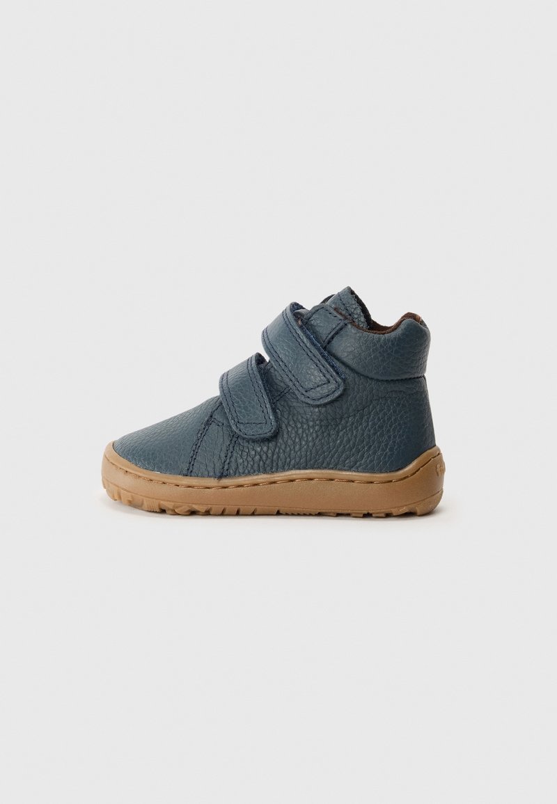 Chaussure bébé en cuir bleu foncé avec deux bandes Velcro réglables et une semelle en caoutchouc marron, vue de côté sur un fond clair.