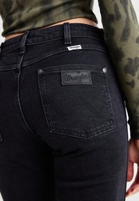 Fekete farmernadrág Wrangler címkével, varrott részletekkel és klasszikus zsebtervezéssel, részletes varrással és fém rögzítőkkel.