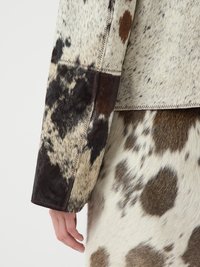 Veste en fausse fourrure avec un design en patchwork dans les tons gris, marron et blanc. Présente une couture à ras et une surface texturée avec des motifs variés inspirés des animaux.