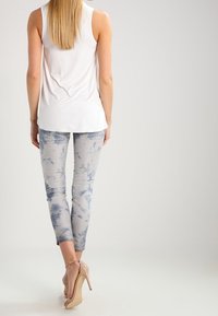 Top blanco sin mangas combinado con jeans ajustados de tie-dye azul claro y sandalias de tacón nude, visto desde atrás.