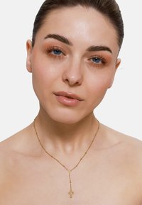 Goldene Halskette mit einem doppelten Kreuzanhänger; filigrane Glieder und glatte Textur betonen das Design. Keine weiteren sichtbaren Accessoires.