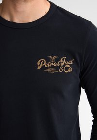 Zwarte longsleeve t-shirt van katoen, met een vintage-stijl gouden logo met een adelaarontwerp op de borst.