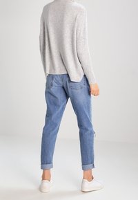 Helle graue, langärmelige Strickjacke kombiniert mit lockeren, mittelblauen Denim-Jeans und weißen Sneakers. Aufgerollte Bündchen an den Jeans sind sichtbar.