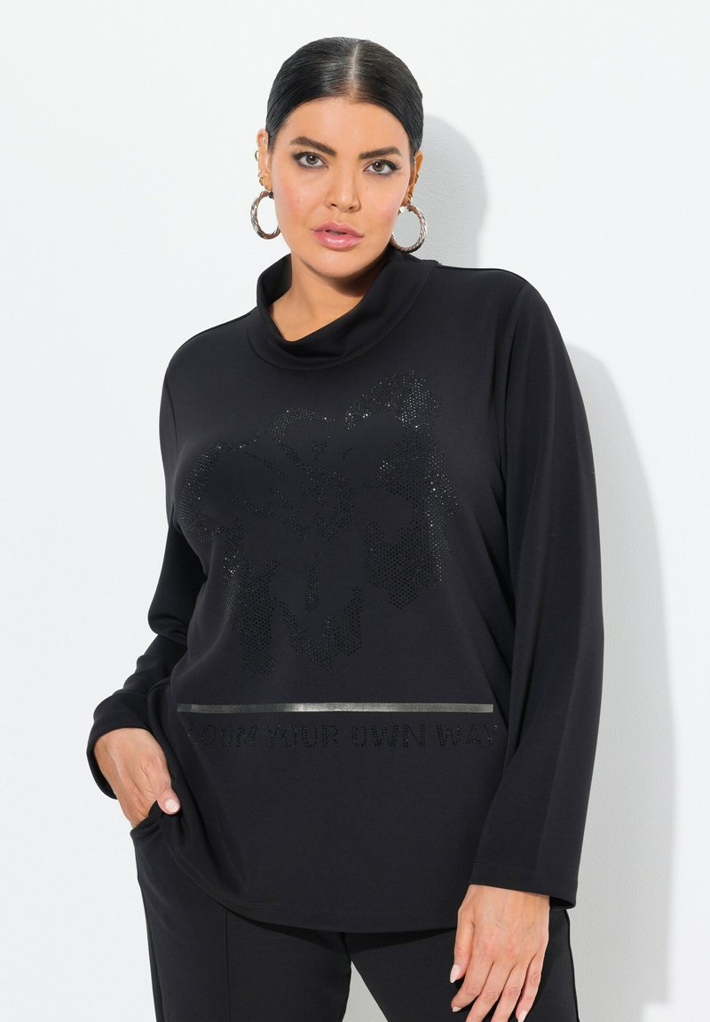 Svart långärmad topp med en cowl-krage, texturerad tyg, paljetter-liknande detaljer och silverfärgad text "BLOOM YOUR OWN WAY."