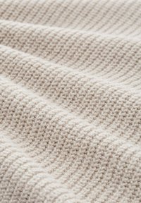 Ljust beige textil med en ribbad struktur, som har mjuka fibrer och subtila nyansvariationer. Närbild visar den intrikata väven.