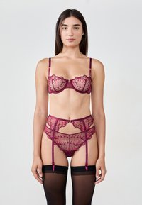 Set di lingerie in pizzo color bordeaux, con bordi ondulati, delicati motivi floreali e una cintura reggicalze abbinata con spalline regolabili e calze nere.
