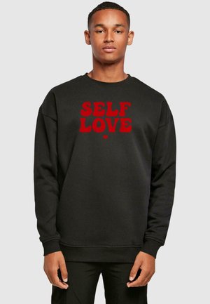 Black sweatshirt with dropped shoulders, featuring bold red text "SELF LOVE" on the front. Made of soft fabric with a classic fit.