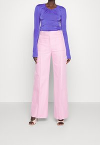 Fialový dlouhý rukáv top s nařasením na výstřihu, spárovaný s růžovými kalhotami s vysokým pasem a širokými nohavicemi. Boty na podpatku s otevřenou špičkou.