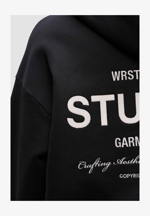 Zwarte hoodie van een katoenmix, met witte borduursels met de tekst "STUDENT" en extra ontwerpelementen op de voorkant.