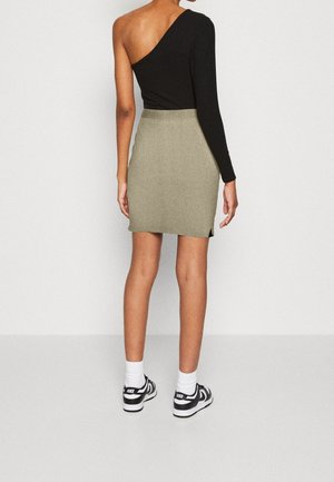 Haut noir à manches longues et à col asymétrique associé à une mini-jupe grise à fines côtes avec des fentes sur les côtés. Des baskets décontractées complètent le look.