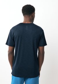 Marineblaues Sport-T-Shirt mit kurzen Ärmeln, einem rundem Ausschnitt und einer strukturierten Stoffoberfläche. Verfügt über eine vertikale Naht am Rücken.