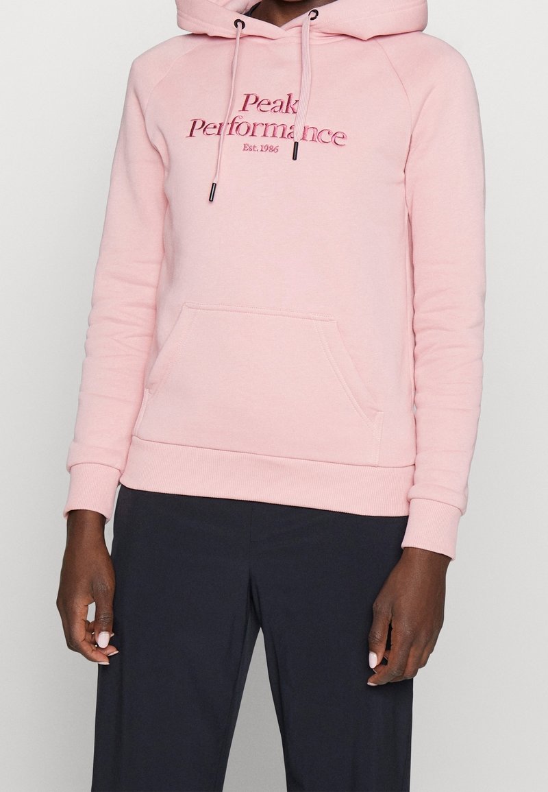 Felpa rosa chiaro realizzata in materiale morbido, con tasca a marsupio frontale, cappuccio con cordino e logo ricamato "Peak Performance".