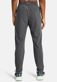 Graue Sporthose mit einem Kordelzugbund, glatter Textur, taillierter Beinform und Taschenverzierungen. Getragen mit gemusterten Laufschuhen.