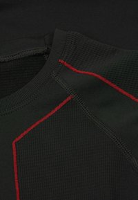 Černé sportovní tričko s texturovanou látkou, červenými švy a kulatým výstřihem. Viditelné švy zvyšují design.