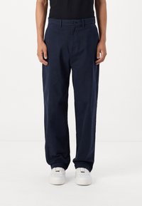 Navy blue cotton trousers with a buttoned waistband, straight-leg design, and side pockets. Worn with white sneakers.