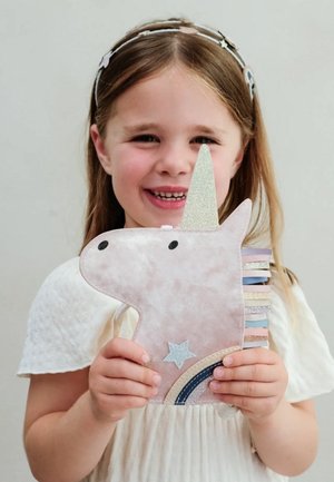 Plush a forma di unicorno rosa con corno glitterato e criniera pastello, caratterizzato da un dettaglio a stella e arcobaleno. Bambina che lo tiene, indossando un vestito bianco.