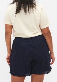 Pantaloni corti blu navy texturizzati con ritagli, caratterizzati da un orlo a onde. Abbinati a una T-shirt leggera di colore neutro.