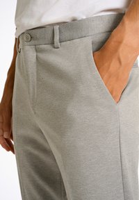 Pantalones de corte entallado en gris claro, hechos de tejido texturizado, con bolsillos inclinados y cierre de botón, terminación lisa y ordenada.