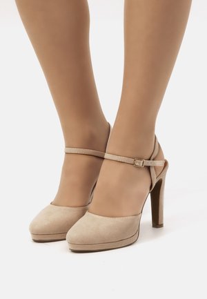 Scarpe con tacco alto in suede beige, con piattaforma, cinturino alla caviglia e dettaglio a fibbia, caratterizzate da una texture liscia e design a punta rotonda.