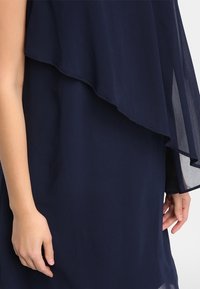 Granatowa, warstwowa sukienka z przezroczystą górną warstwą i solidną dolną warstwą. Charakteryzuje się luźnym krojem i miękką teksturą materiału.