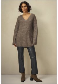 Bruine, oversized gebreide trui met een V-halsontwerp, gecombineerd met hoge zwarte leren broeken en bruine enkellaarsjes. Gladde textuur.