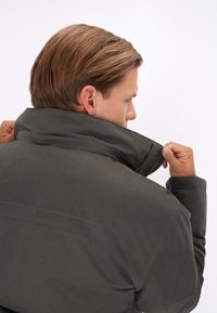 Donkergrijze waterdichte jas met een hoge kraag, ritssluiting en een gladde textuur. Heeft een eenvoudig ontwerp en stiksels.