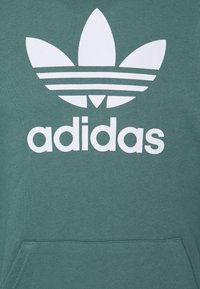 Bluza z kapturem w kolorze morskim z dużym białym logo adidas i trzema paskami. Gładka faktura, przednia kieszeń oraz ściągacz na dole.