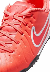 Scarpa da calcio rossa brillante con tomaia sintetica testurizzata, tre file di lacci e logo Swoosh bianco di Nike. Suola in gomma nera per la trazione.