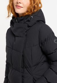 Chaqueta de plumas negra con un alto cuello, diseño acolchado y capucha ajustable. Presenta un parche de logo en la manga y tela texturizada.