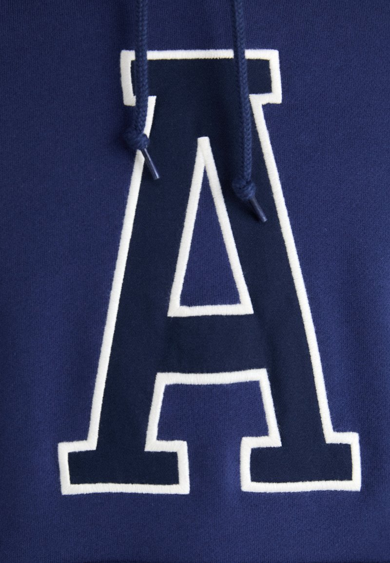 Blaues Sweatshirt mit einem großen, weiß umrandeten Buchstaben "A" in der Mitte, das eine weiche Textur und passende Kordelzugakzente bietet.