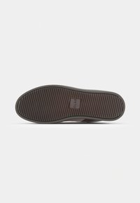 Semelle de chaussure en caoutchouc brun avec une texture à motifs, comportant des rainures horizontales et un logo rectangulaire embossé. Forme plate et arrondie.