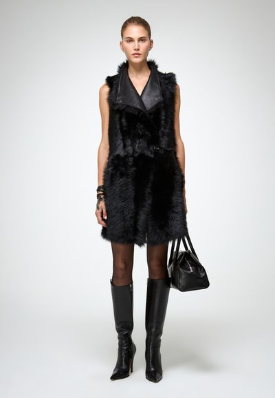 Juodas dirbtinio kailio chalatas su odinėmis apykaklėmis, su susiaurintu liemeniu ir dvigubo užsegimo dizainu. Dėvimas su juodais aukštiems auliniais bateliais.