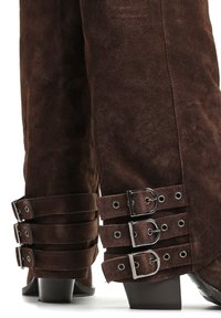 Brązowe zamszowe botki o zwężającym się fasonie, z wieloma regulowanymi skórzanymi paskami z metalowymi klamrami w okolicy kostki oraz blokowym obcasem.