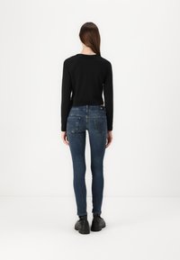Mustapaita pitkillä hihoilla yhdistetty tummansinisillä skinny-farkuilla. Farkuissa on koristeompeleet ja tarra takataskussa. Mustat kengät viimeistelevät asun.