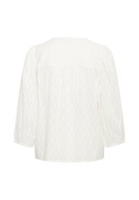 Chemisier blanc à manches longues, en tissu texturé avec un motif ondulé subtil. Encolure ronde et détails froncés aux manches.