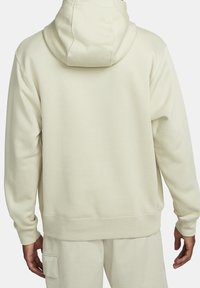 Krämfärgad hoodie med dragsnodd, ribbade muddar och nederkant. Slätt tyg med en avslappnad passform och minimala sömmar på baksidan.