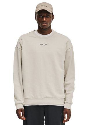 Beige sweatshirt med rund hals og subtil 'HALO' logo. Båret med en matchende beige kasket. Blødt stof og afslappet pasform. Mørke bukser fuldender looket.