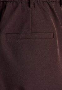 Temno rjave tkaninske hlače z enim zadnjim žepom z ravnim dizajnom in subtilno teksturo. Elastičen pas za udobje.