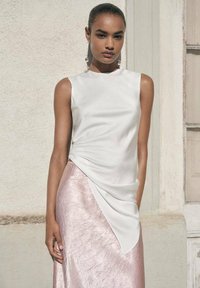 White sleeveless top made of smooth fabric paired with a pink, textured skirt featuring an asymmetrical hemline and shiny finish.