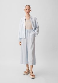 Camicia azzurra chiara con taglio rilassato, chiusura frontale con bottoni e maniche lunghe. Abbinata a pantaloni azzurri chiari a gamba larga e sandali con piattaforma beige.